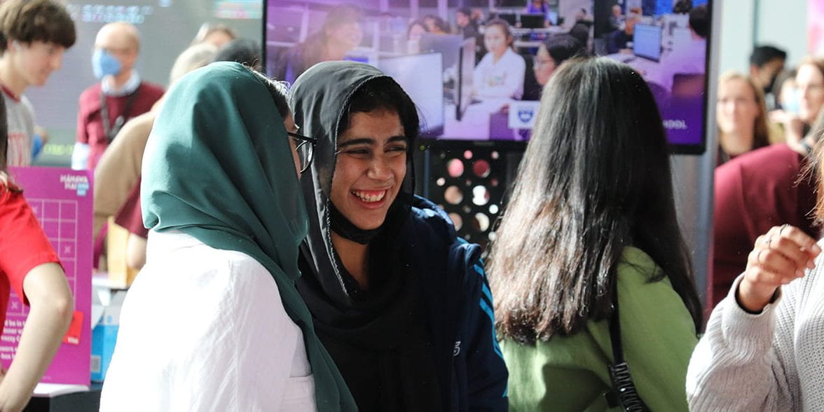 Two women smiling together in a crowd of students