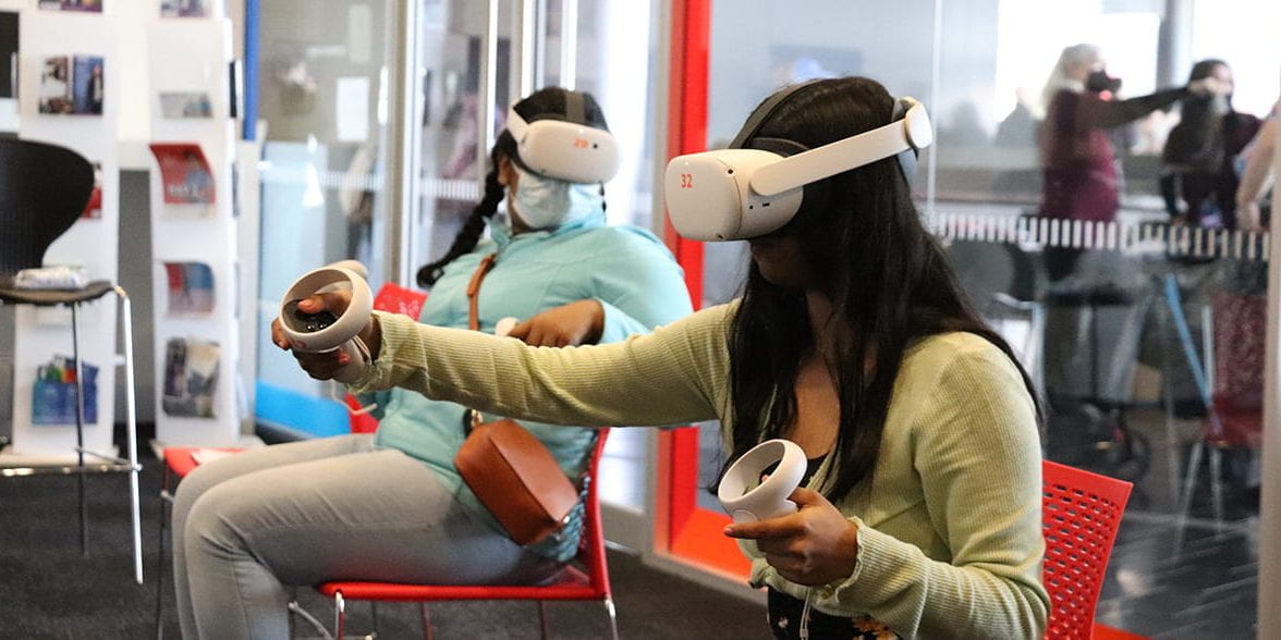Two students wearing virtual reality headsets sit on chairs